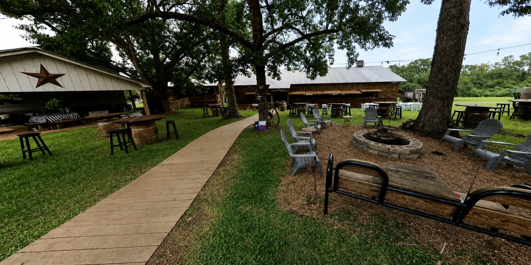 Fire pit, barrel tables, and boardwalks under the oaks at the heart of camp